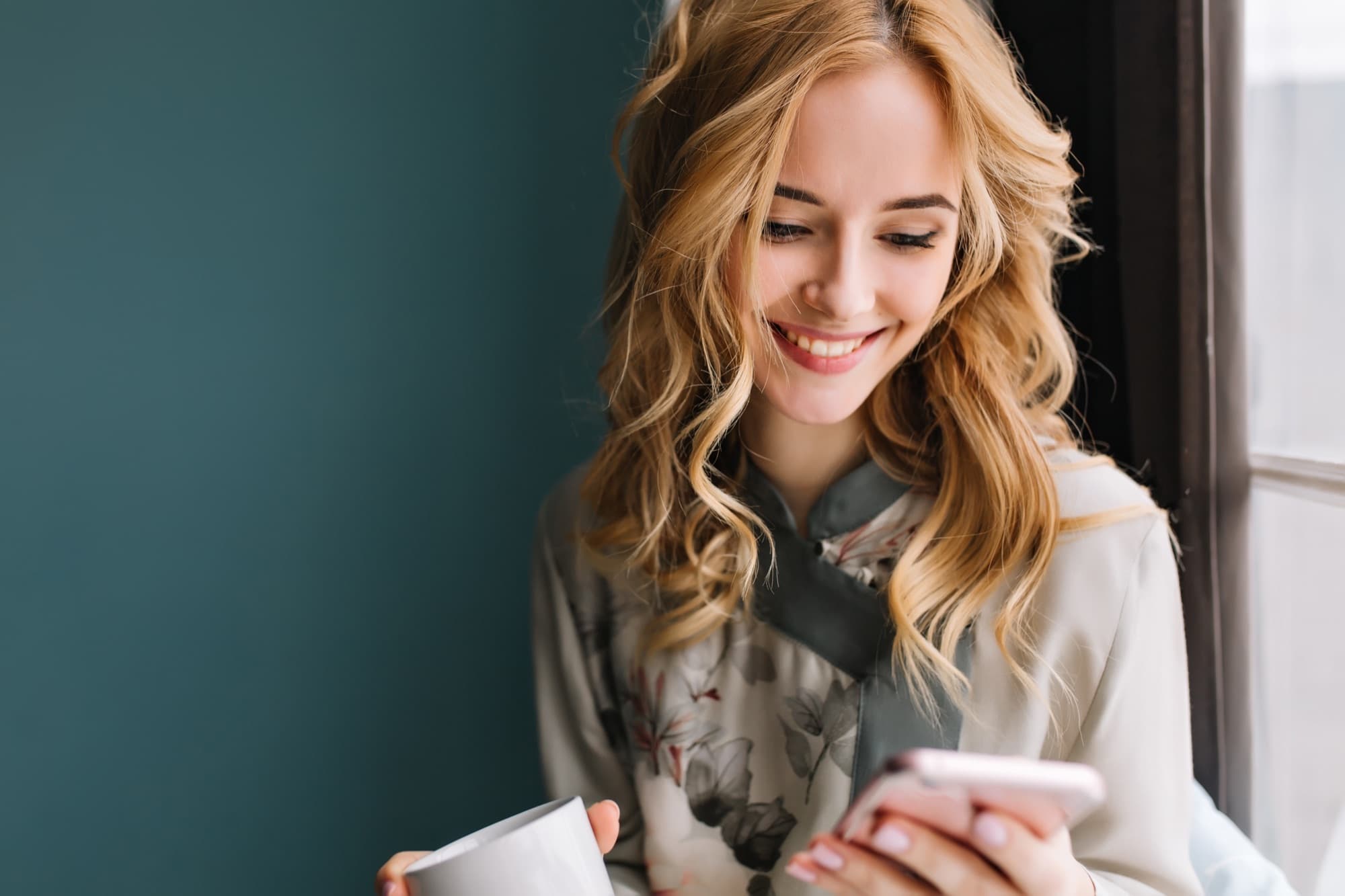 Femme souriante avec son téléphone et un café